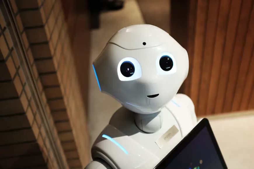 A white humanoid robot with a tablet beside a wooden wall.